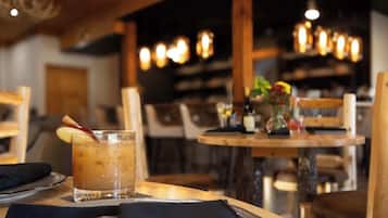 A restaurant interior with wooden tables and chairs, a glass of iced beverage with a straw, and a vase with flowers on the table.