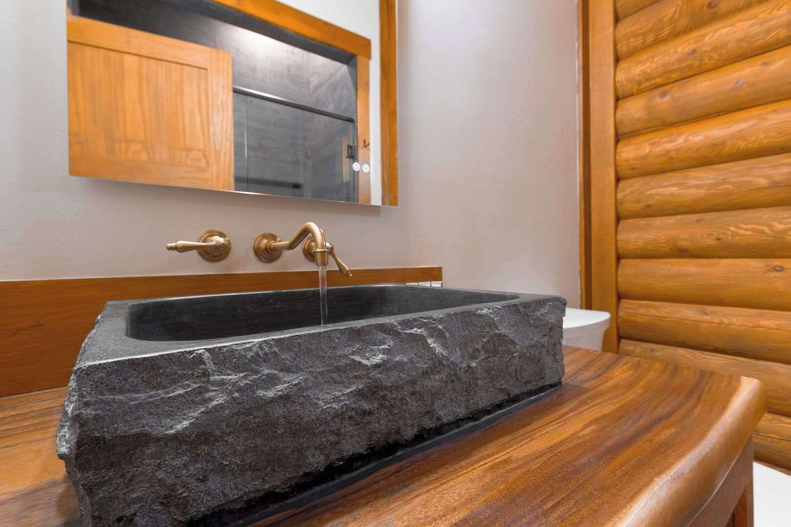Un lavabo de piedra con un grifo de latón en un baño rústico de madera.