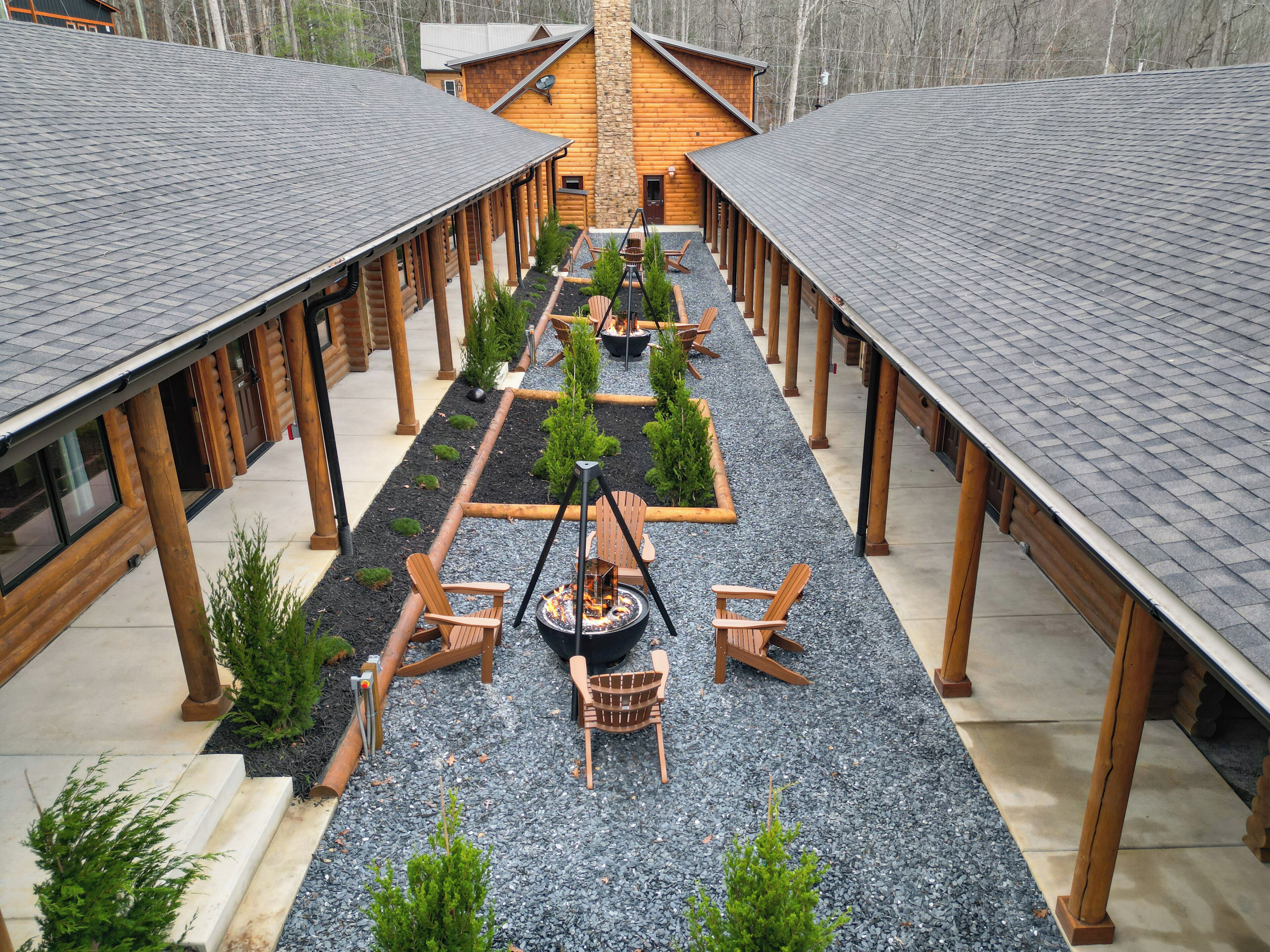 A log cabin with a covered outdoor seating area, fire pit, and small trees.