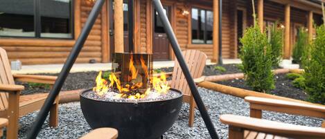 A fire pit with chairs around it, set on gravel, in front of a wooden building with windows.