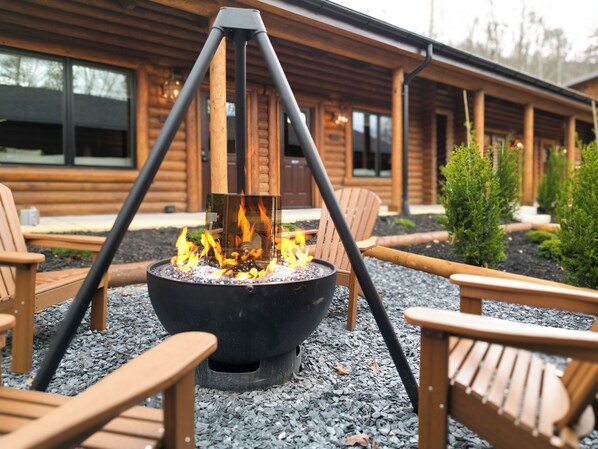 A fire pit with chairs around it, set on gravel, in front of a wooden building with windows.