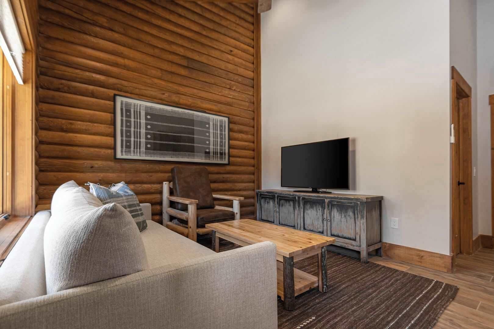 Een blokhut interieur met een bank, fauteuil, houten salontafel en een televisie op een kast.