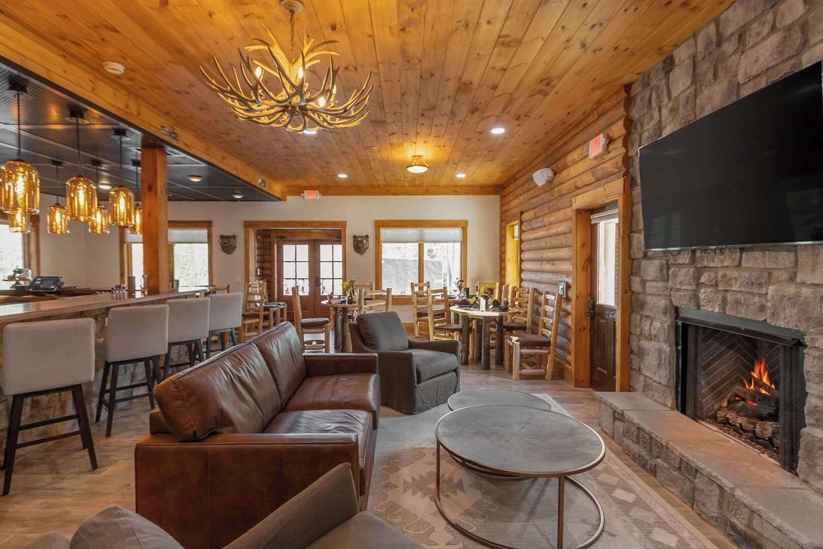 A cozy lodge interior with a stone fireplace, leather seating, a bar area, and a dining space.