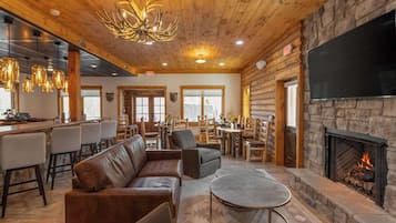 A cozy lodge interior with a stone fireplace, leather seating, a bar area, and a dining space.