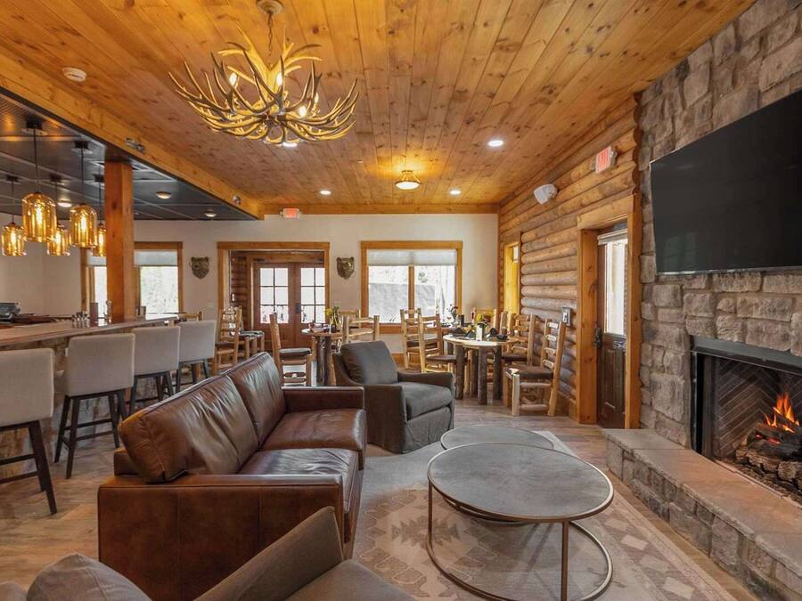 A cozy lodge interior with a stone fireplace, leather seating, a bar area, and a dining space.