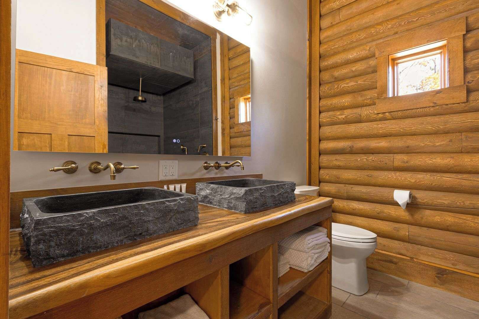 Une salle de bain avec deux vasques en pierre, un meuble-lavabo en bois, un miroir et des toilettes.