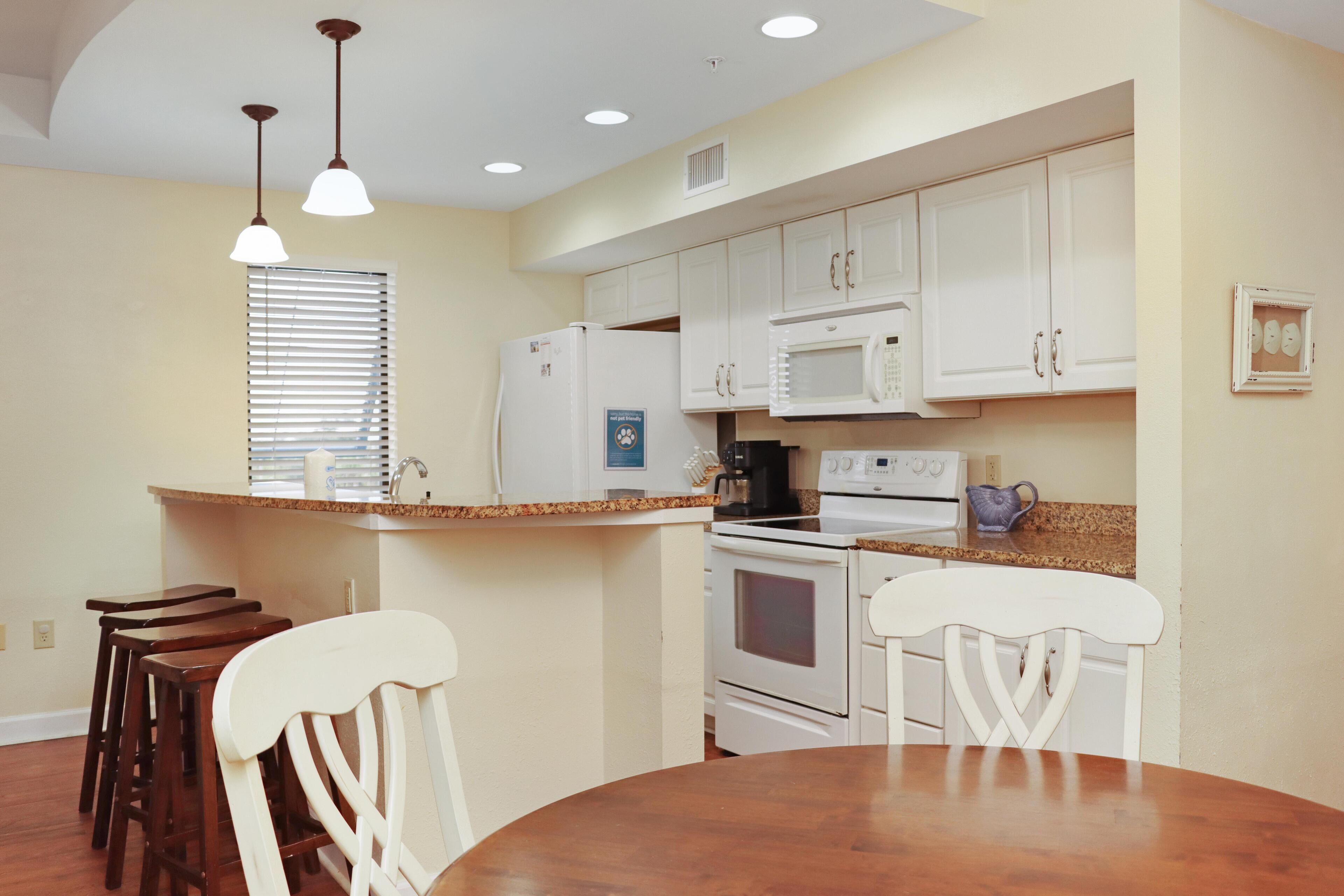 A kitchen with white cabinets, a microwave, a stove, and a dining area with a wooden table and chairs.