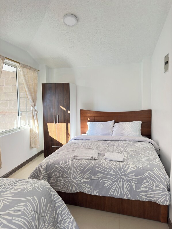 A bedroom with a bed, a wardrobe, and a window with curtains.