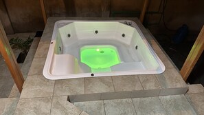 Relax in a spacious hot tub with a flat bottom and central drain, surrounded by a potted plant.