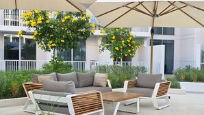 An outdoor seating area with a sofa and chairs, a table, and a large umbrella providing shade.
