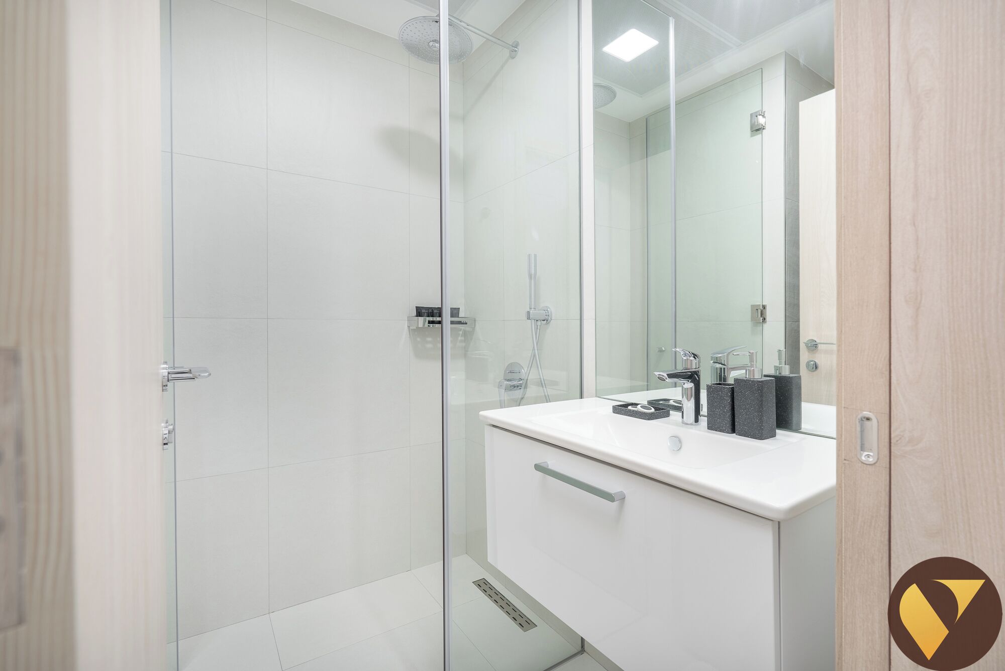 A modern bathroom with a glass shower enclosure, a white vanity with a mirror, and a sink.