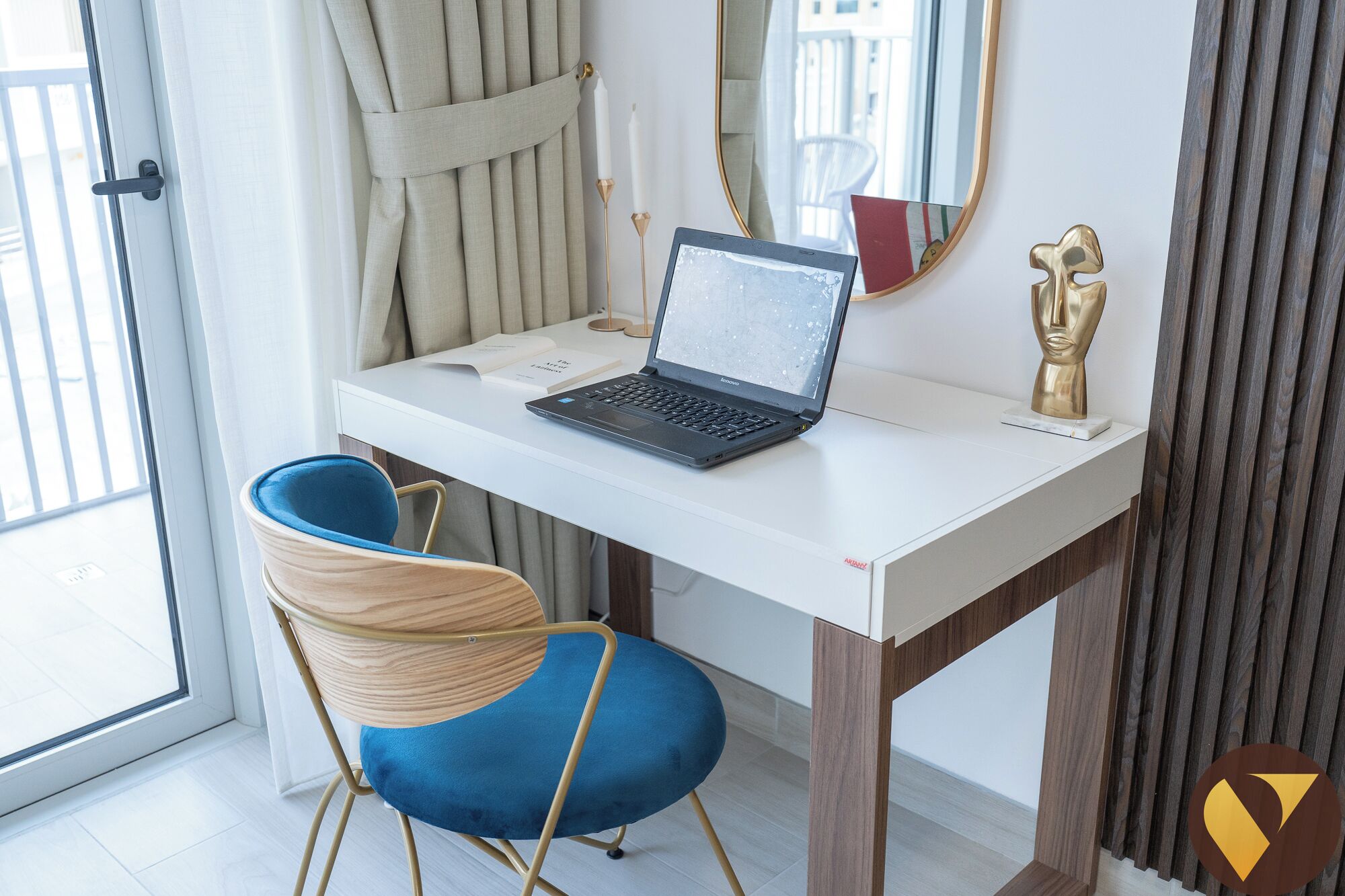 A modern office space with a laptop on a white desk, a blue chair, a gold statue, and a mirror on the wall.