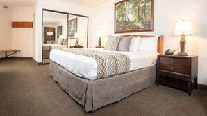 A hotel room with a large bed, a nightstand with a lamp, a painting on the wall, and a mirror.