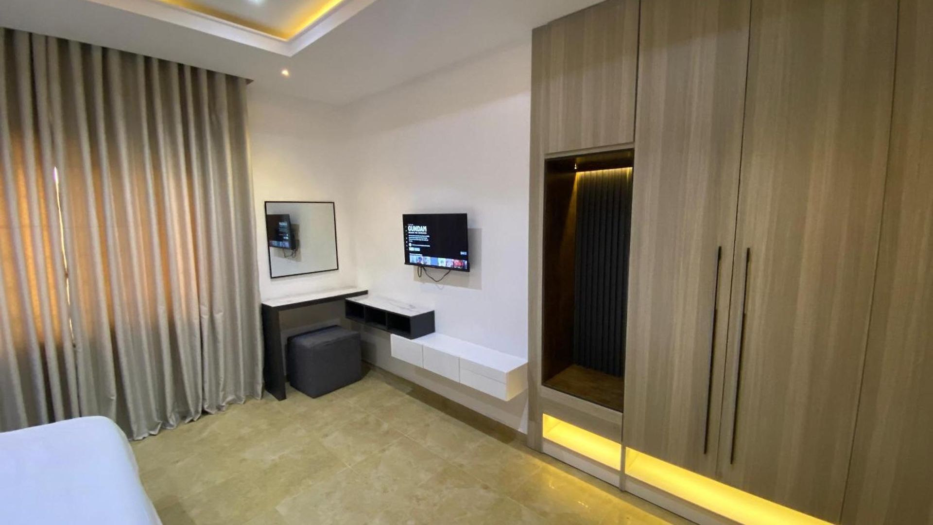 A modern hotel room with a large bed, a desk with a chair, a television mounted on the wall, and a wardrobe with a mirror.