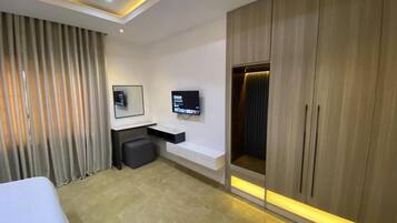 A modern hotel room with a large bed, a desk with a chair, a television mounted on the wall, and a wardrobe with a mirror.