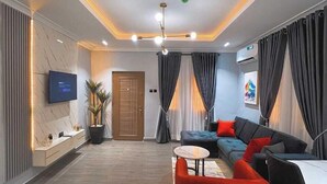 Ein modernes Wohnzimmer mit einer Couch, einem roten Sessel und einem an der Wand befestigten Fernseher.