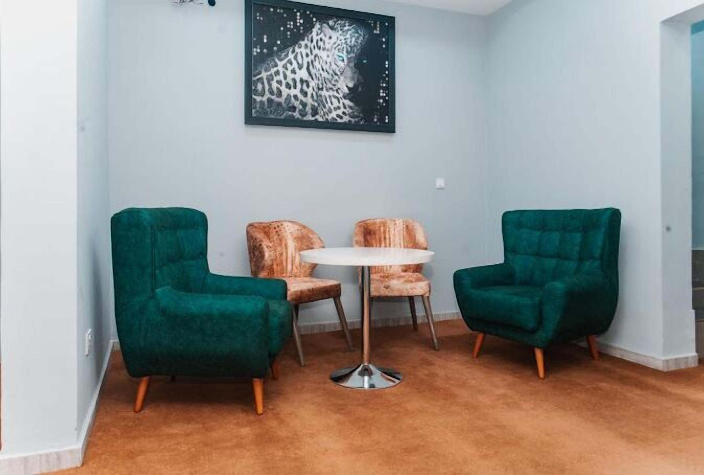 A room with two green armchairs, a small round table, and a leopard print chair.