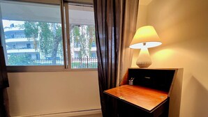 A hotel room with a wooden desk, a lamp, a radiator, and a window with curtains. - 5 min to Parc des Princes • Studio 18 m²<br>Boulogne (Boulogne-Billancourt)