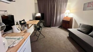 A compact living space with a kitchenette, a TV, a sofa, and a curtain separating the living area from the bedroom. - 5 min to Parc des Princes • Studio 18 m²<br>Boulogne (Boulogne-Billancourt)