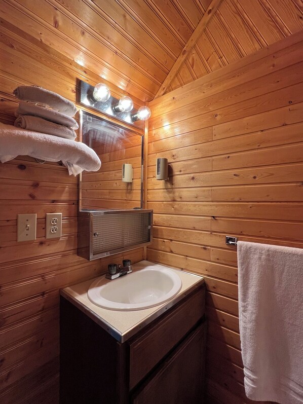A wooden cabin bathroom with a sink, mirror, and towel rack. - Tal-Adventures Lodge (Skwentna)
