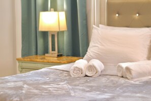 A neatly made bed with rolled white towels, a bedside lamp, and a green curtain.