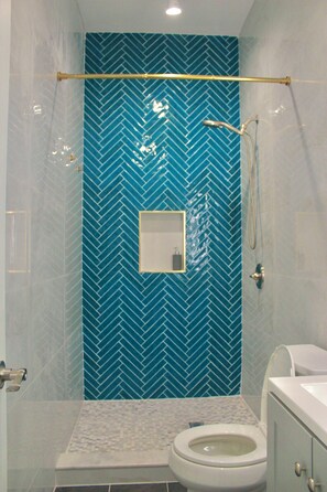 Ein Badezimmer mit blauen Fischgrätfliesen, einer weißen Toilette und einem Duschbereich mit goldener Duschstange.