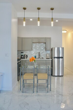 A modern kitchen with a stainless steel refrigerator, a coffee maker, and a glass table with chairs. - 15 Minutes From Manhattan Private Two Bedroom Apartment in Astoria/LIC/Queens NY (Queens)