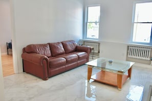 A spacious room with a brown leather sofa and a glass-top coffee table. - 15 Minutes From Manhattan Private Two Bedroom Apartment in Astoria/LIC/Queens NY (Queens)