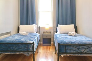 Ein Doppelzimmer mit zwei Betten, einem Nachttisch und einem Fenster mit Vorhängen.