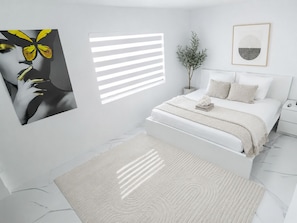 A modern bedroom with a bed, bedside tables, a nightstand, a potted plant, and artwork on the walls.