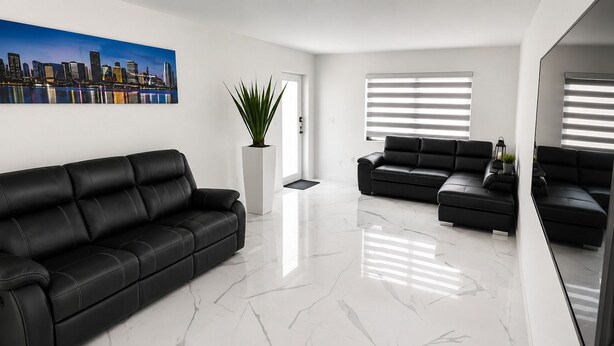 Un salon moderne avec un canapé en cuir noir, un canapé plus petit, une plante en pot et un tableau représentant un paysage urbain accroché au mur.
