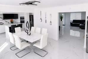 A modern kitchen with a dining area, white furniture, and a flat-screen TV.