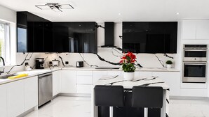 Une cuisine moderne avec des meubles noirs, un plan de travail en marbre et un îlot central doté de chaises.