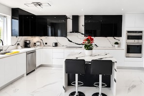 A modern kitchen with black cabinets, a marble countertop, and a central island with chairs.