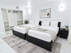 A modern bedroom with two beds, a walk-in closet, and a bedside table with a lamp.