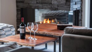 A cozy living room with a stone fireplace, a wooden table with a bottle of wine and two glasses, and a comfortable sofa.