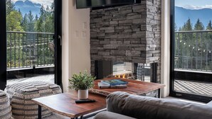 A cozy living area with a stone fireplace, comfortable seating, and a large window offering a mountain view.