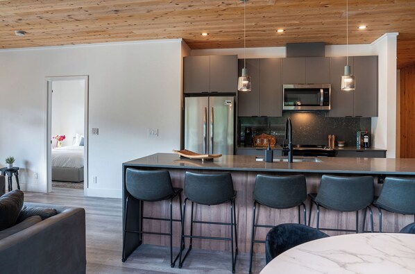 A modern kitchen with a central island, bar stools, and a dining area. - The Begbie Penthouse (Revelstoke)