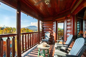 Une terrasse en bois offrant une vue sur les montagnes, avec une table et deux chaises Adirondack.