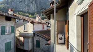 A narrow street with buildings, a washing machine visible in a window, and a mountainous backdrop.