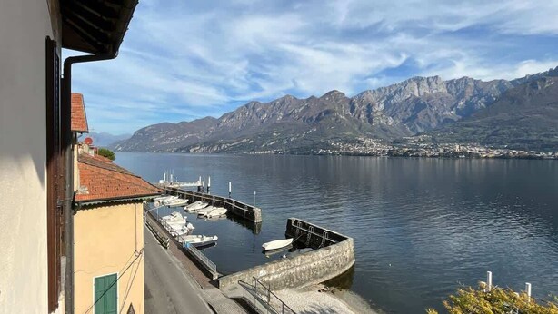 A waterfront view with mountains in the background, a dock with boats, and a building with a red roof.
