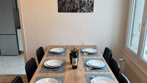 Une table à manger dressée avec des assiettes, des verres et une bouteille de vin, entourée de chaises noires.