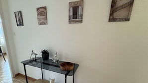 Un couloir avec une table à plateau de verre, une plante en pot, une petite figurine et un banc en bois.