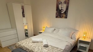 Une chambre à coucher comprenant un lit, un banc, des tables de chevet et un grand tableau accroché au mur.