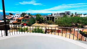 Ein Balkon mit Blick auf eine Küstenstadt, darunter Häuser und ein klarer, blauer Himmel.