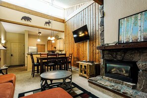 Un salon chaleureux avec une cheminée, des murs en bois, un téléviseur et un coin repas.