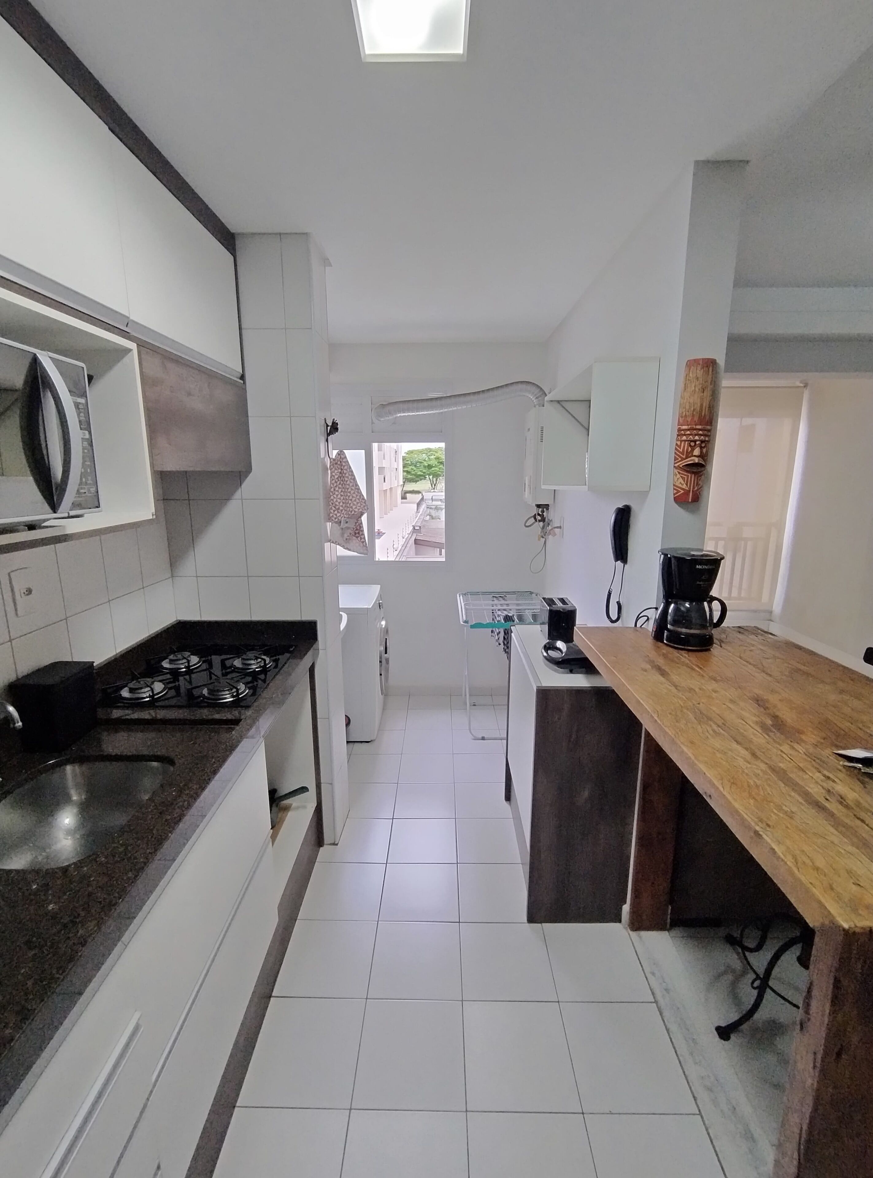 Een moderne keuken met witte kasten, een gasfornuis, een magnetron, een koffiezetapparaat en uitzicht buiten door een raam.