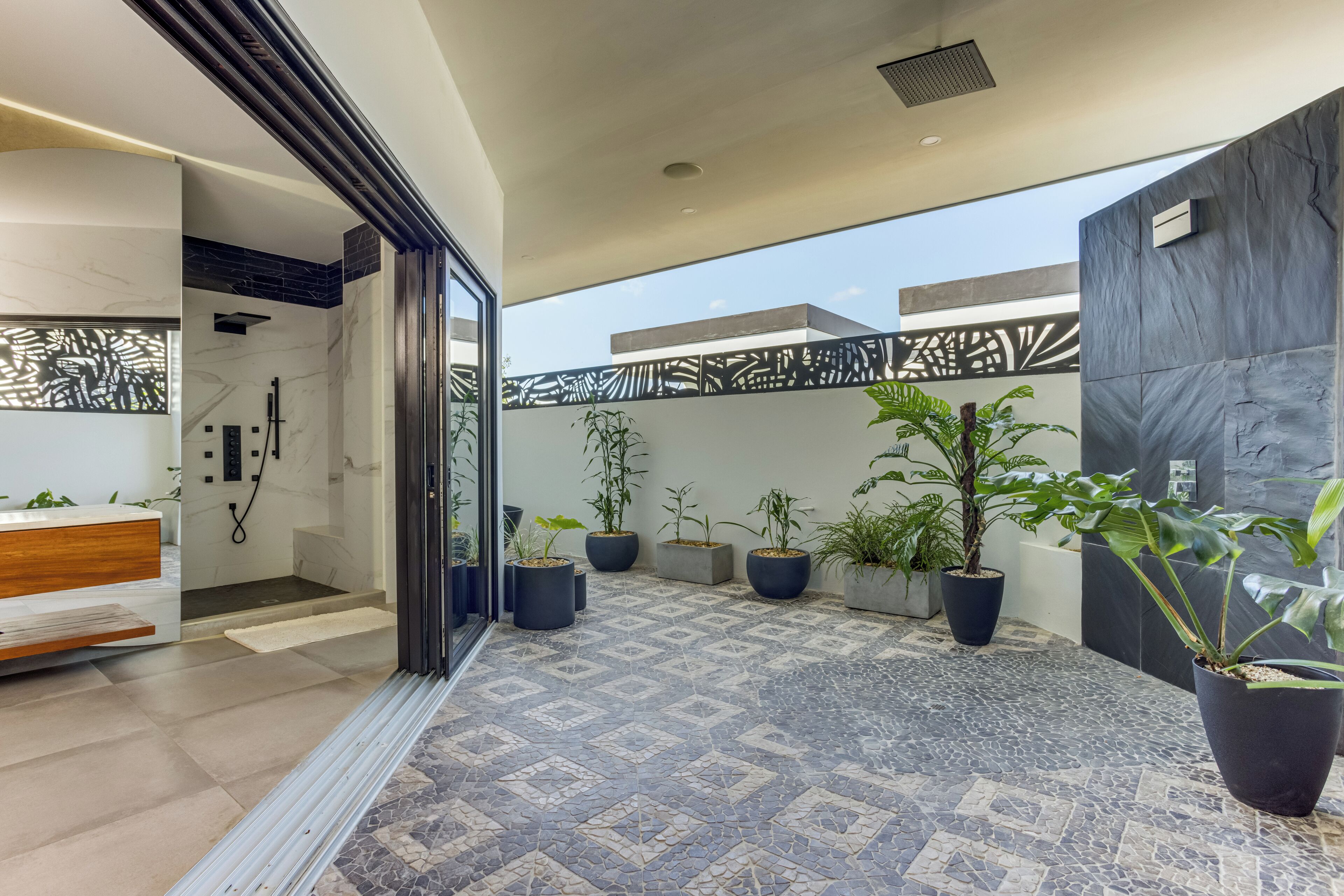 A modern bathroom with a shower, a wooden vanity, and potted plants.
