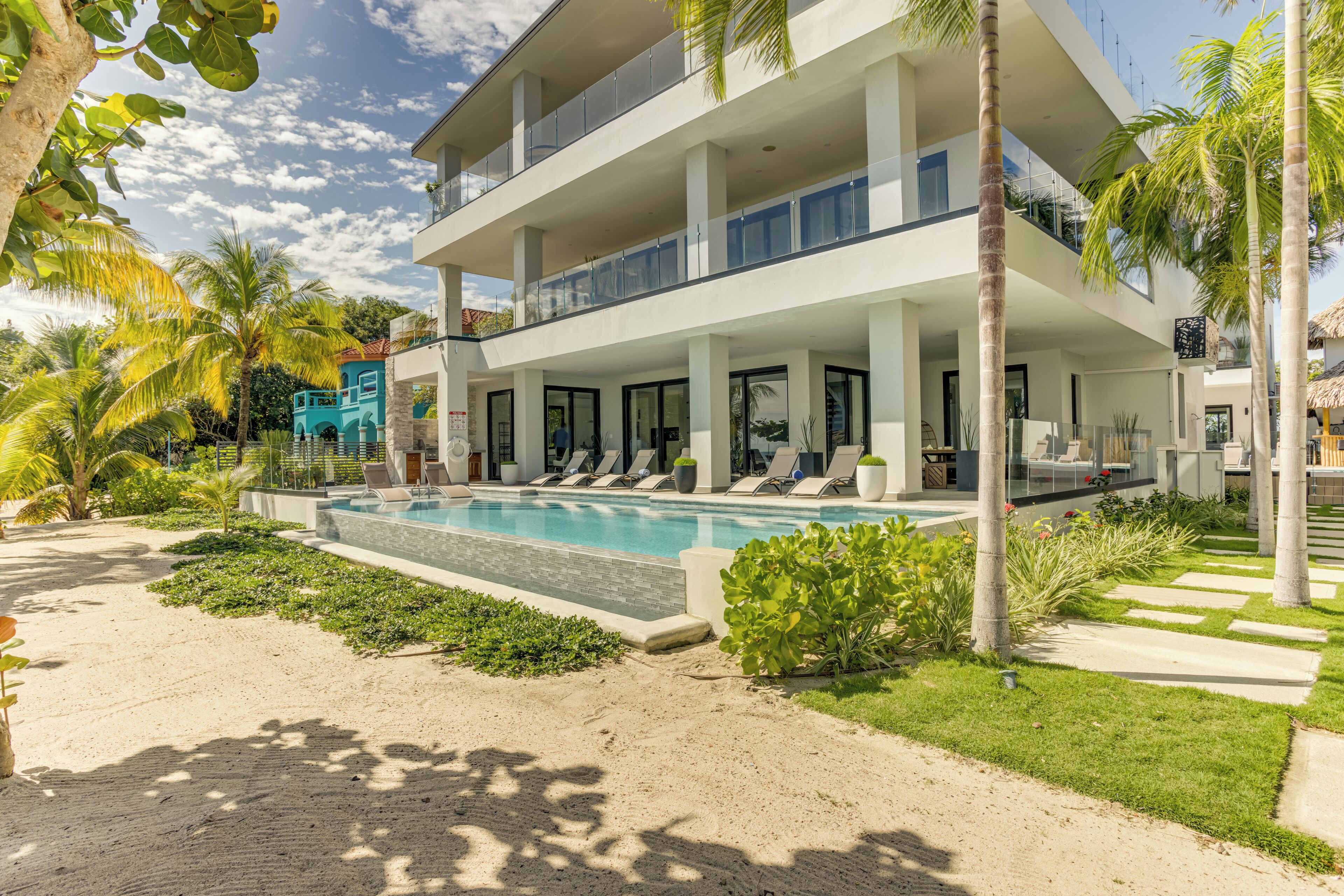 Un hotel moderno de varios pisos con piscina, palmeras y vistas a la playa.