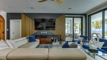 A modern living room with a large beige sectional sofa, a glass coffee table, and a ceiling fan.